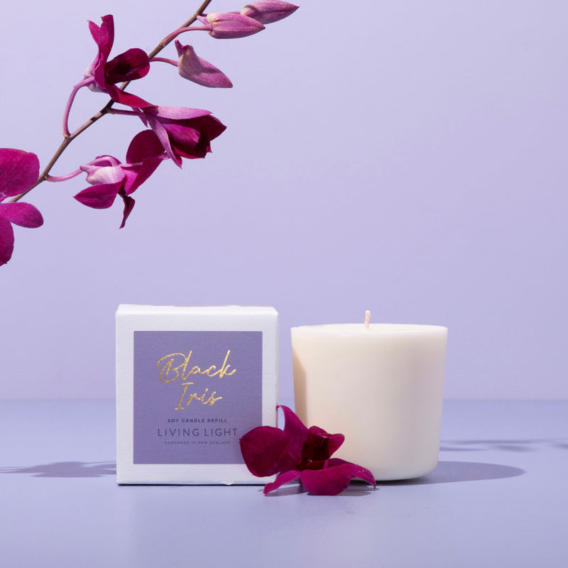 Soy candle on purple background with black iris flowers.. 100% soy wax candle. Premium black iris scent. Living Light Candles.