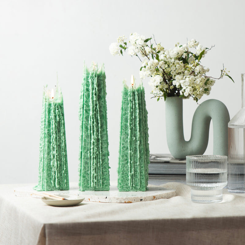 Living Light Festive Pine Icicle Candles burning in a serene setting with fresh flowers and glassware, showcasing their signature lace-like wax drips.