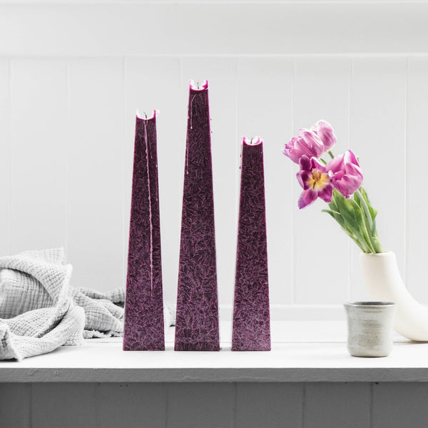 Trio of tall plum-coloured icicle wax candles from Living Light NZ, styled with soft linen and fresh tulips on a white shelf.