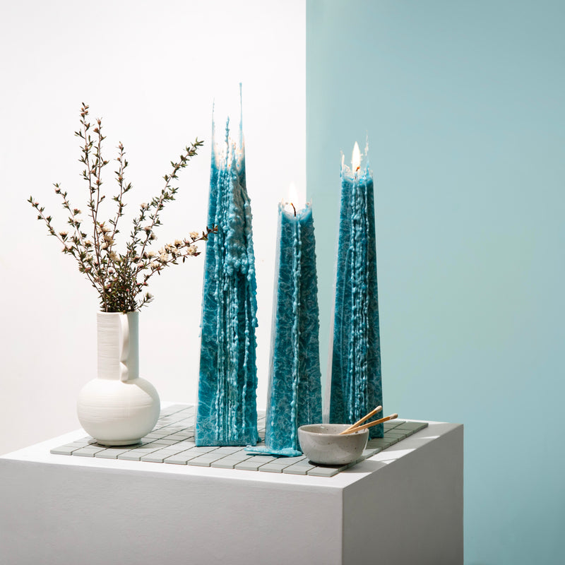 Living Light Ocean Sage Icicle Candles in aqua blue, burning with sculptural wax drip detail. Styled with ceramic decor and native florals.