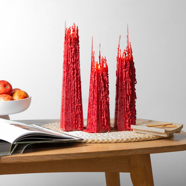 Living Light Pohutukawa red icicle candles burning on a wooden table, showcasing their signature sculptural wax drip design.