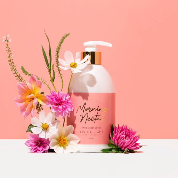 Living light morning nectar body and hand lotion. pink background, white surface with pink, yellow and white flowers 